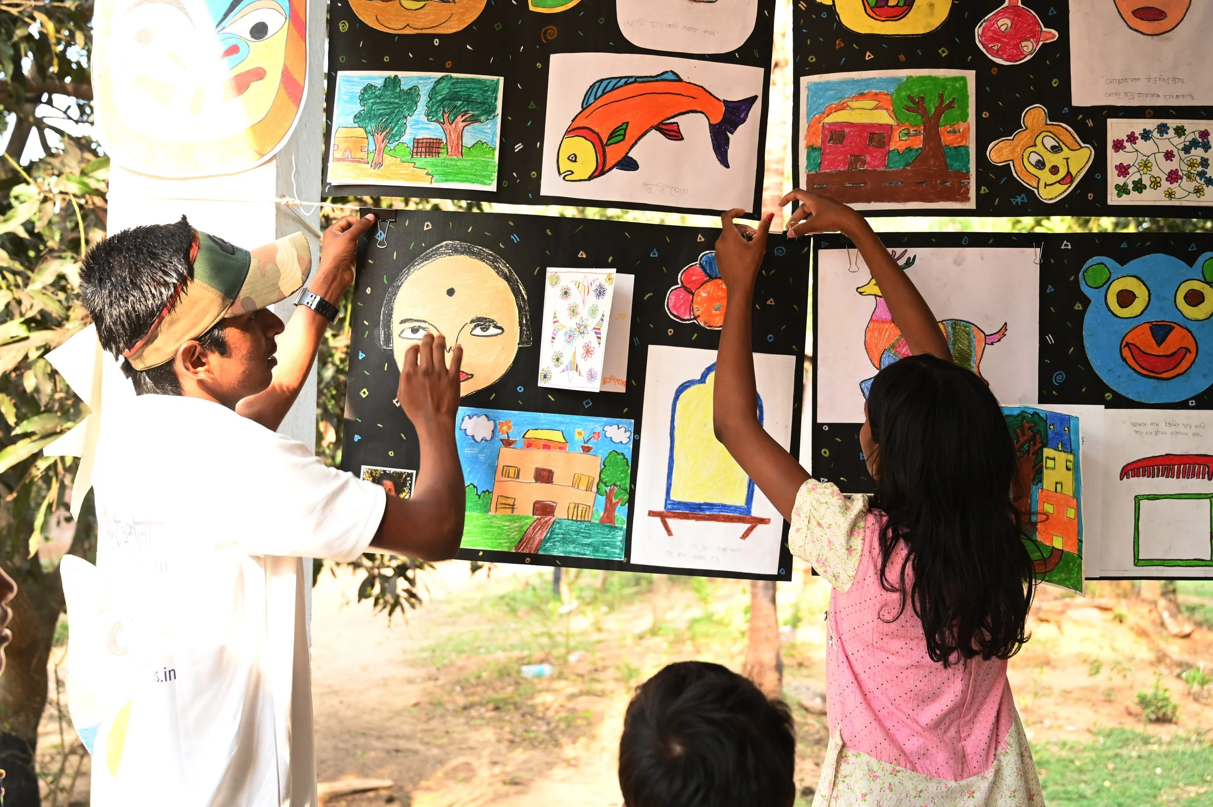 Children and adults hanging and arranging colorful children's artwork on outdoor display boards.