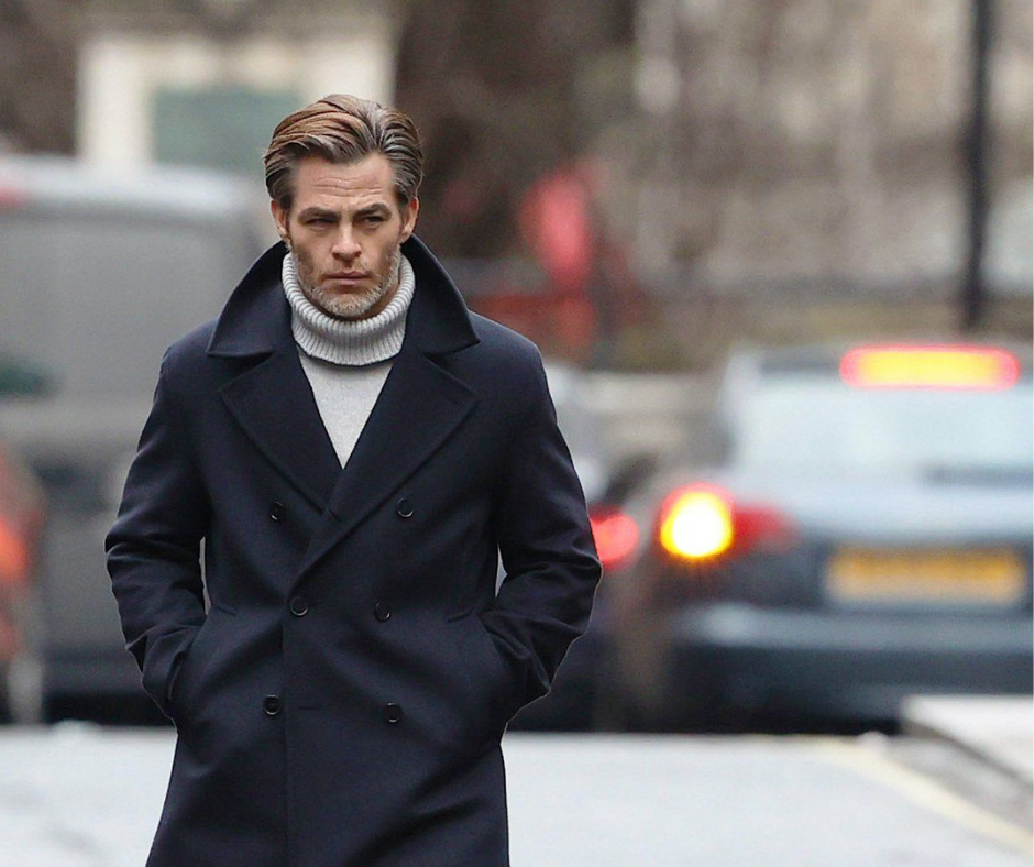 Scene from All the Old Knives (2022): Chris Pine in dark peacoat and light turtleneck walking outdoors with blurred cars in the background.