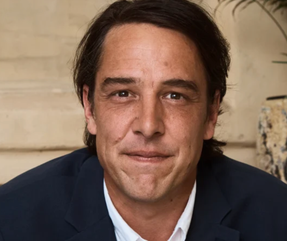 Samuel Johnson headshot in navy blazer against a neutral backdrop.
