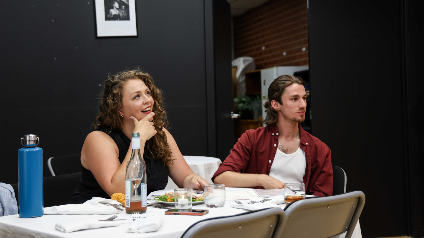 Two actors seated at a dinner table during a Howard Fine Acting Studio Masterclass scene, reacting during an ensemble performance.