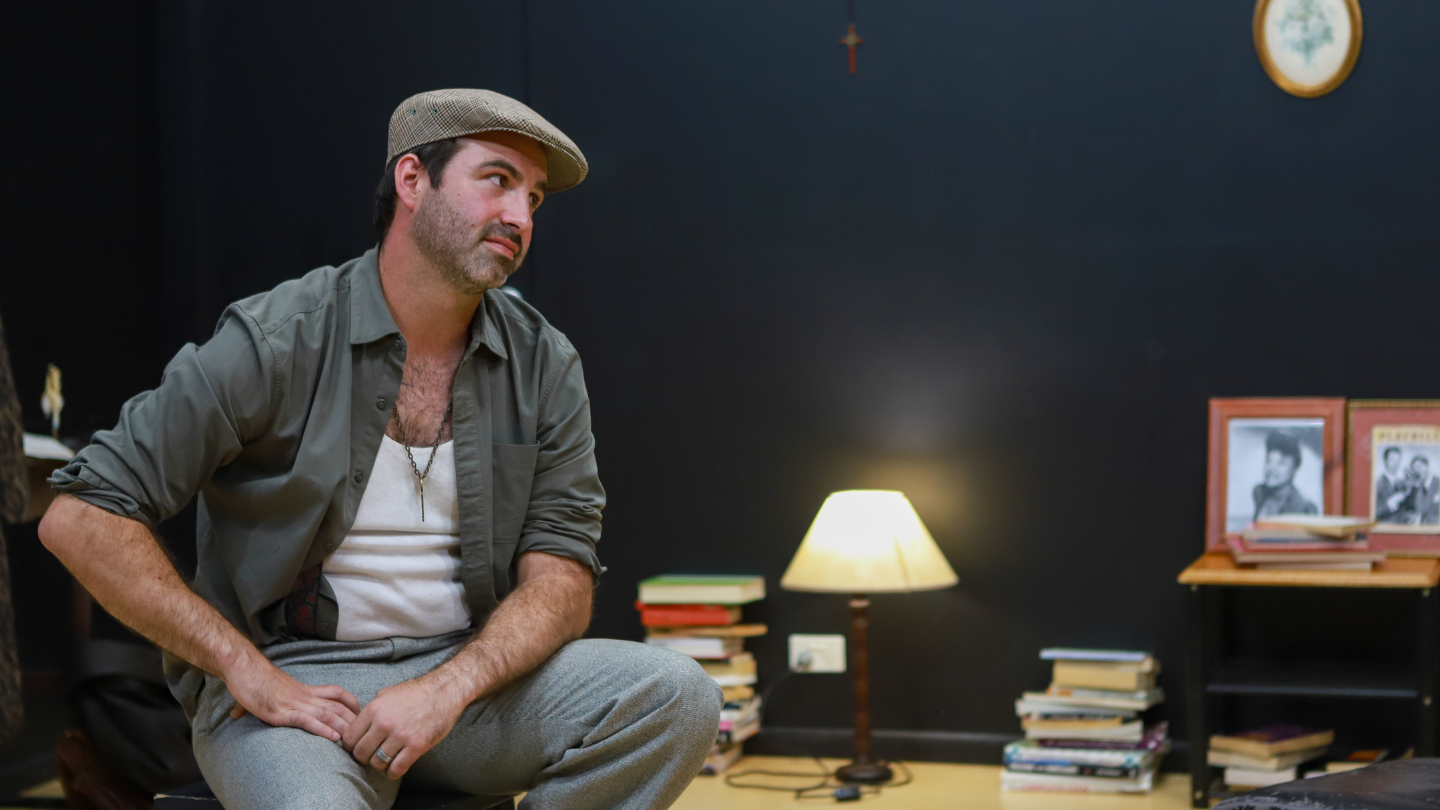 Actor seated in a dramatic scene setup during the Howard Fine Acting Studio Masterclass, surrounded by practical set elements and warm lighting.