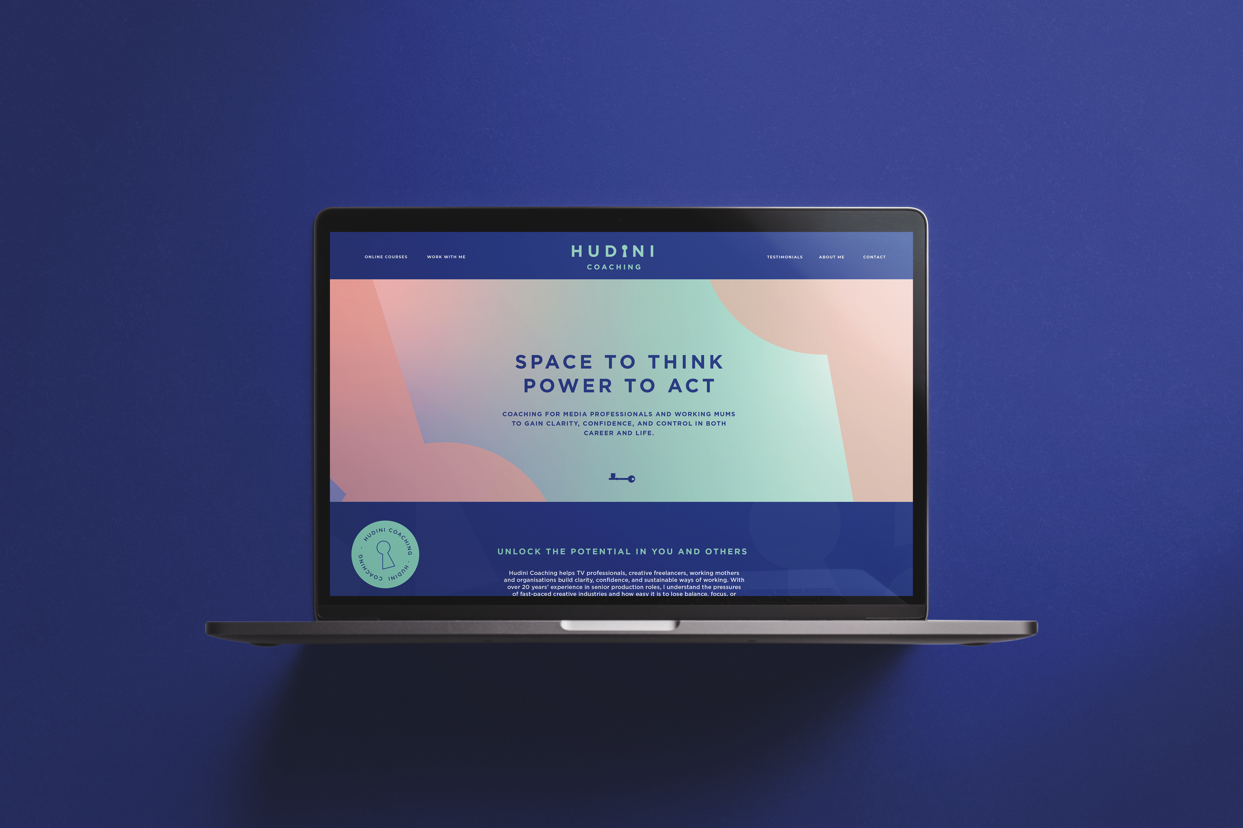 A laptop displaying a coaching website called Hudini Coaching on a dark blue surface.