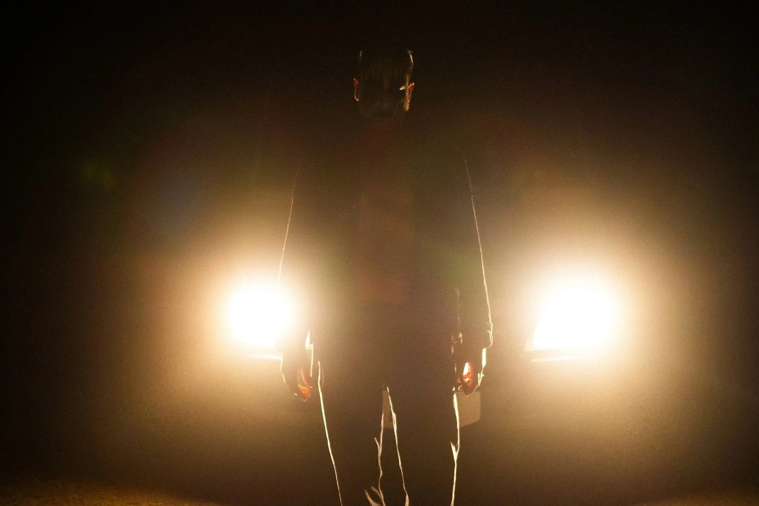 Person standing in dark environment with bright lights behind them, silhouette effect, facing forward.