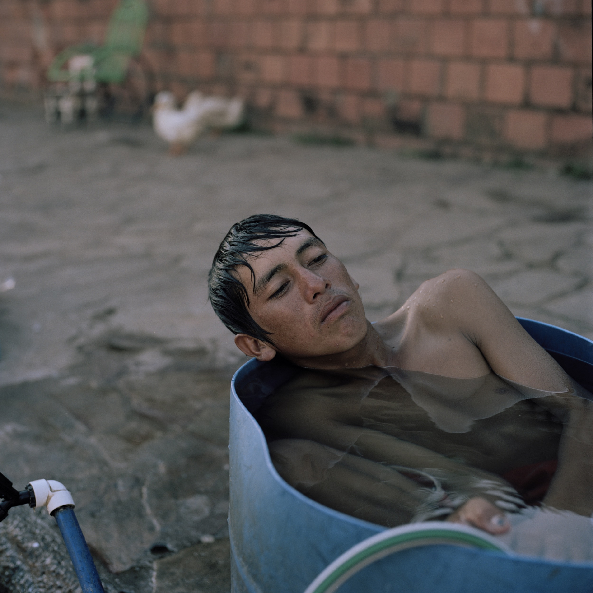 Juan Ramón, 16, takes a bath on a barrel in front of their makeshift home in the streets of Asunción where he has been for eight months together with his family. They were living in the “bañado”, the area surrounding the river until recent floods resulting from El Niño, as well as deforestation due to agribusiness further up the river forced them to evacuate.