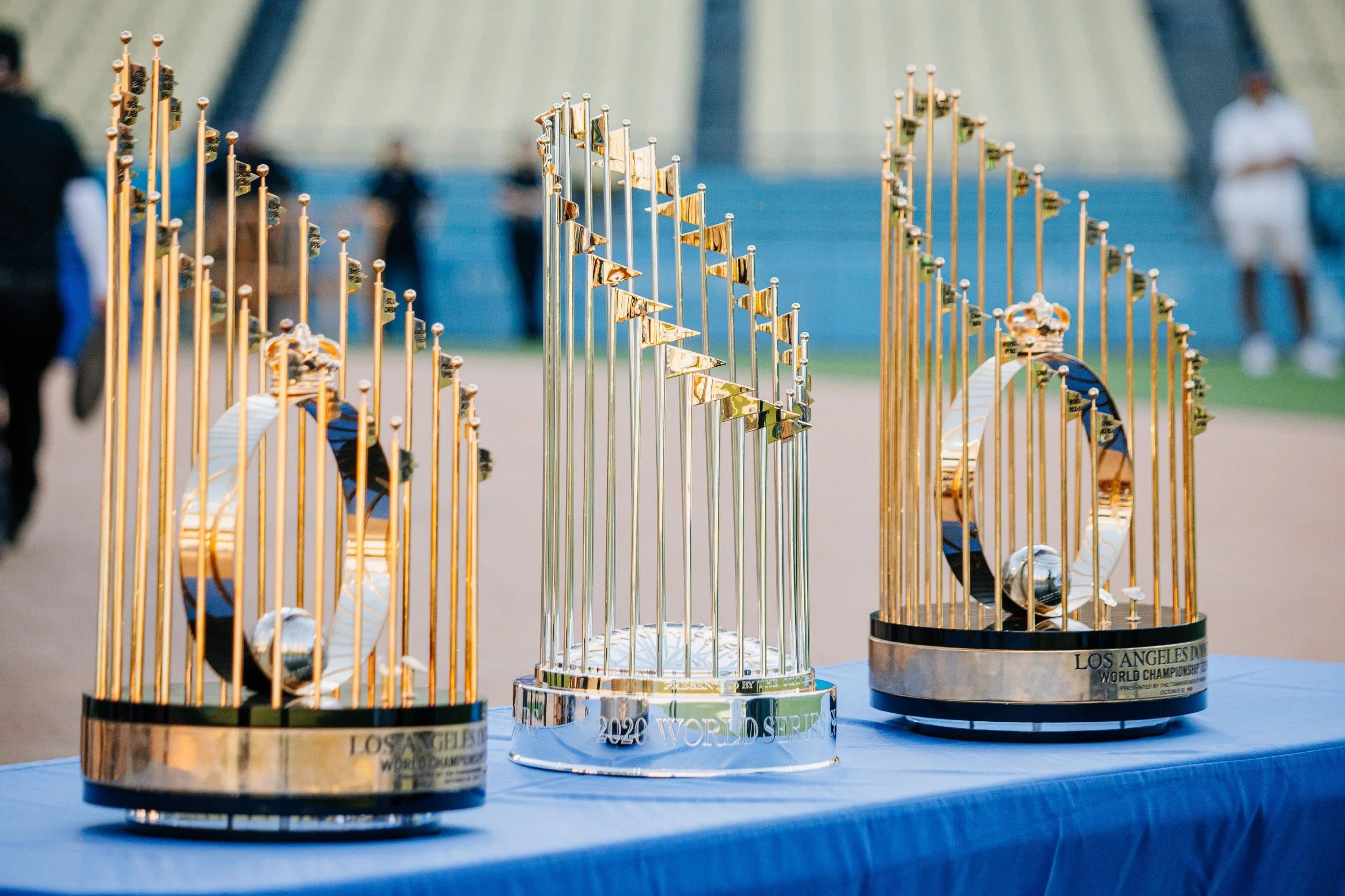 Three trophies for the 2020 World Series Baseball Champions on a blue tablecloth, with a sports stadium in the background.