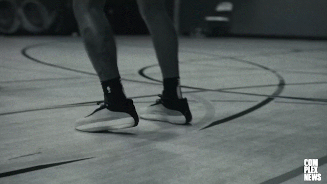 Close-up of a person's athletic legs and feet, wearing black sneakers, on a gymnasium basketball court.