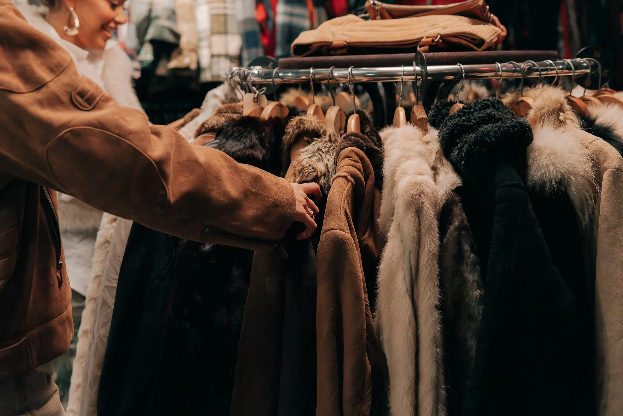 People shopping for and browsing winter coats and faux fur accessories at a clothing store.
