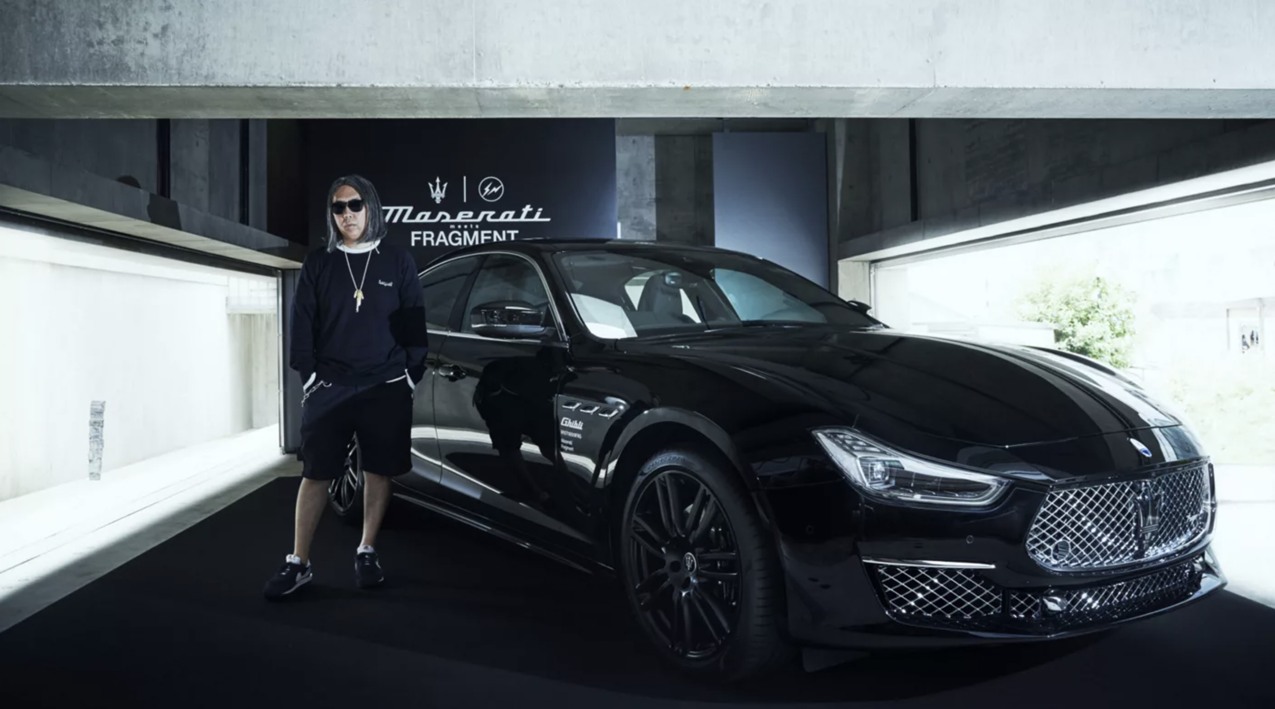 A man standing next to a black luxury sports car in an indoor showroom with a Maserati sign in the background.