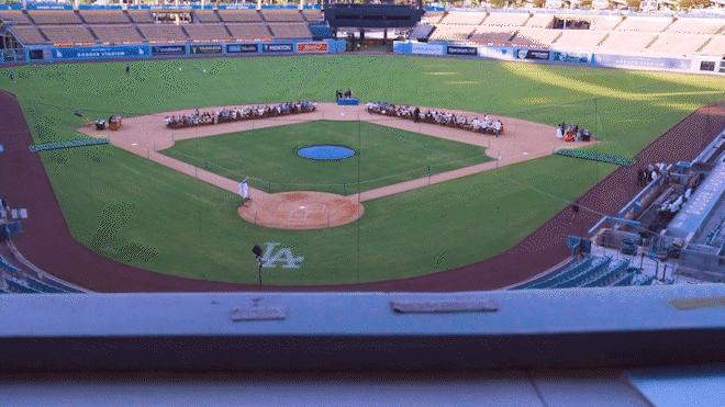 Empty baseball stadium with the field prepared for a game, and people seated on the field.