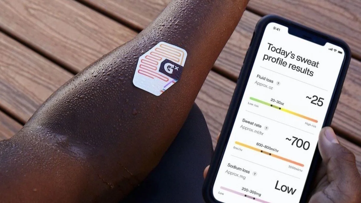 A person’s arm with a sweat sensor sticker on it next to a smartphone displaying a sweat profile report, showing fluid loss, sweat rate, and sodium loss.