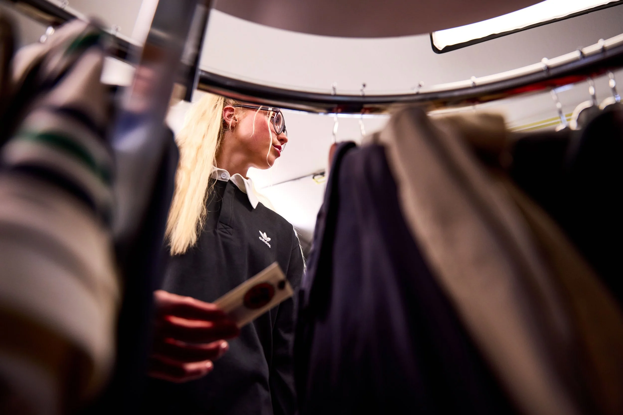 A woman with blonde hair and glasses looking at clothing on a rack in a store.