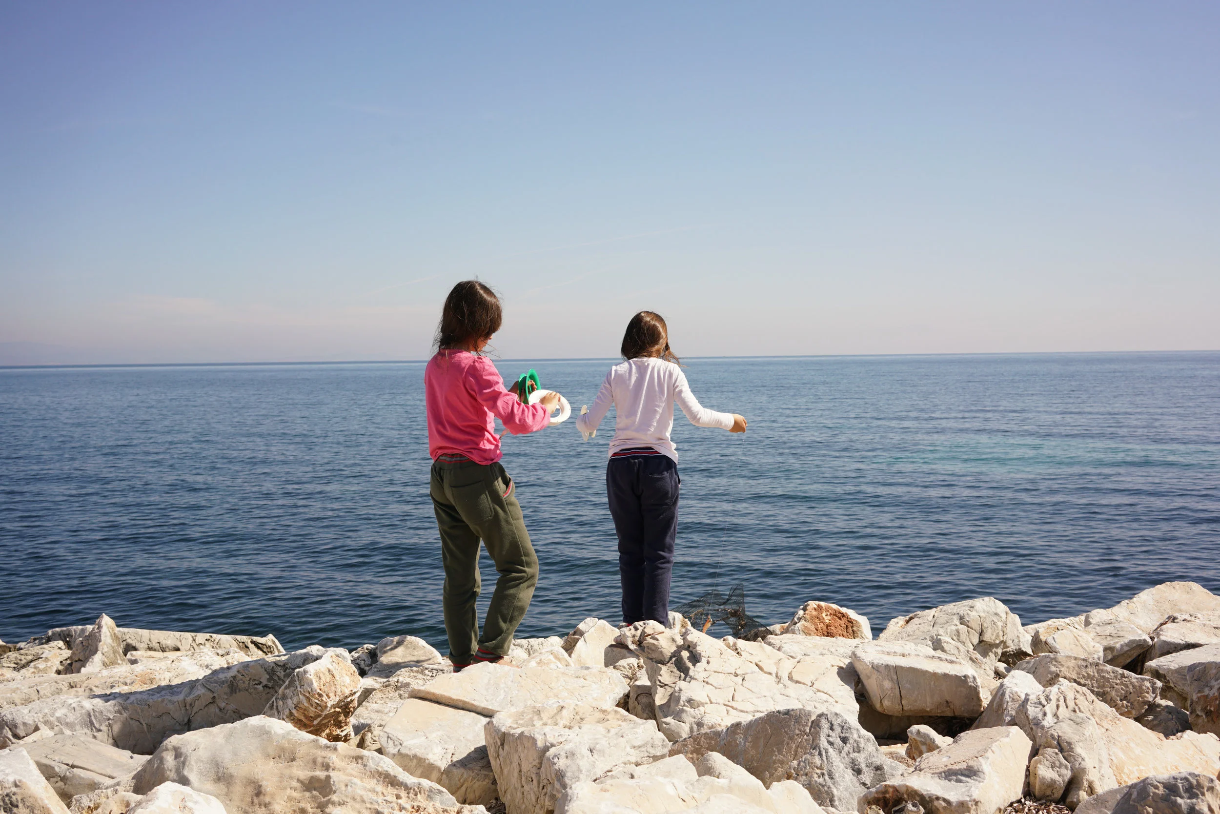 The twin sisters untangle their fishing wire in the early morning sun. Their family fled Iraq in early 2016. Lesbos, Greece. April 2017. 