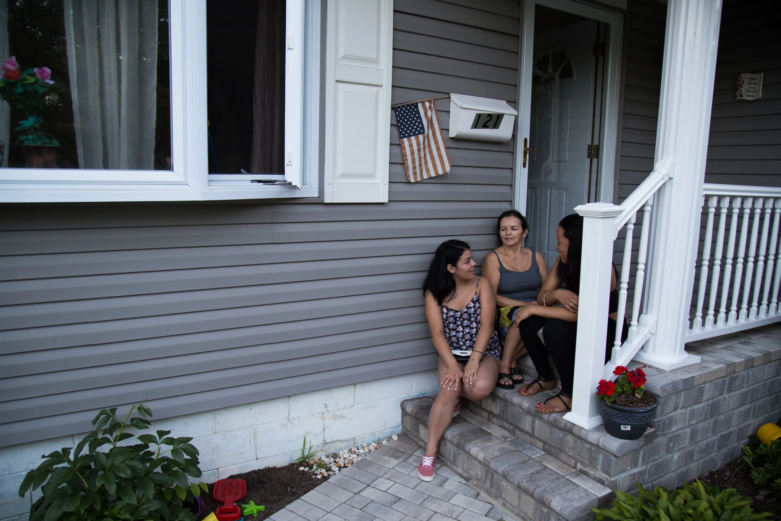 Eliana Sabogal, 18, (from left), her grandmother Luz Sanabria, 63, and her friend Natacha Castillo, 19, sit on the porch of Sabogal's family home in Southampton, NY, on August 3, 2015. Saboga works at a McDonald's in the summer to earn money that helps sustain her family in the winter.