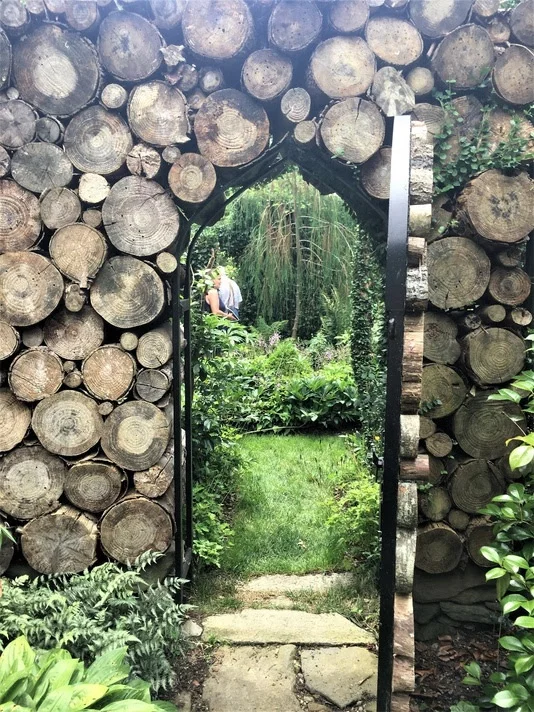 The log wall frames a view into a garden of green.