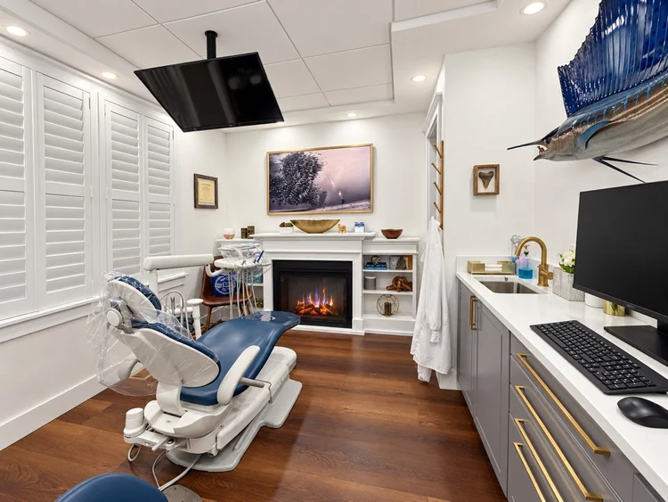 Dental hygiene room at our San Marco office with a ceiling-mounted TV and a fireplace with art above it