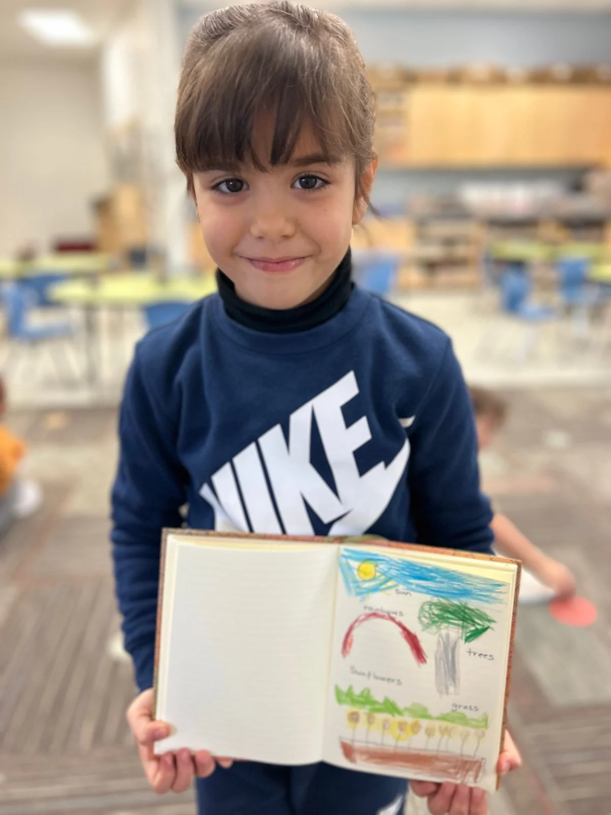 Student displaying a Gratitude Journal drawing of a sunny landscape with a rainbow