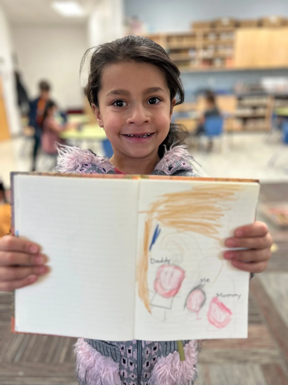 Smiling student holding her Gratitude Journal open to a colorful drawing of her family