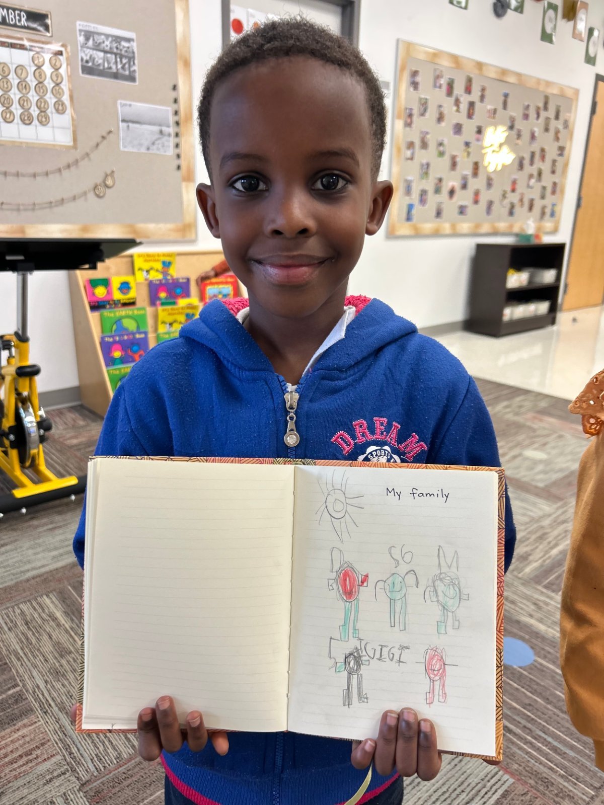 Young student in a navy polo shirt holding up her Gratitude Journal drawing