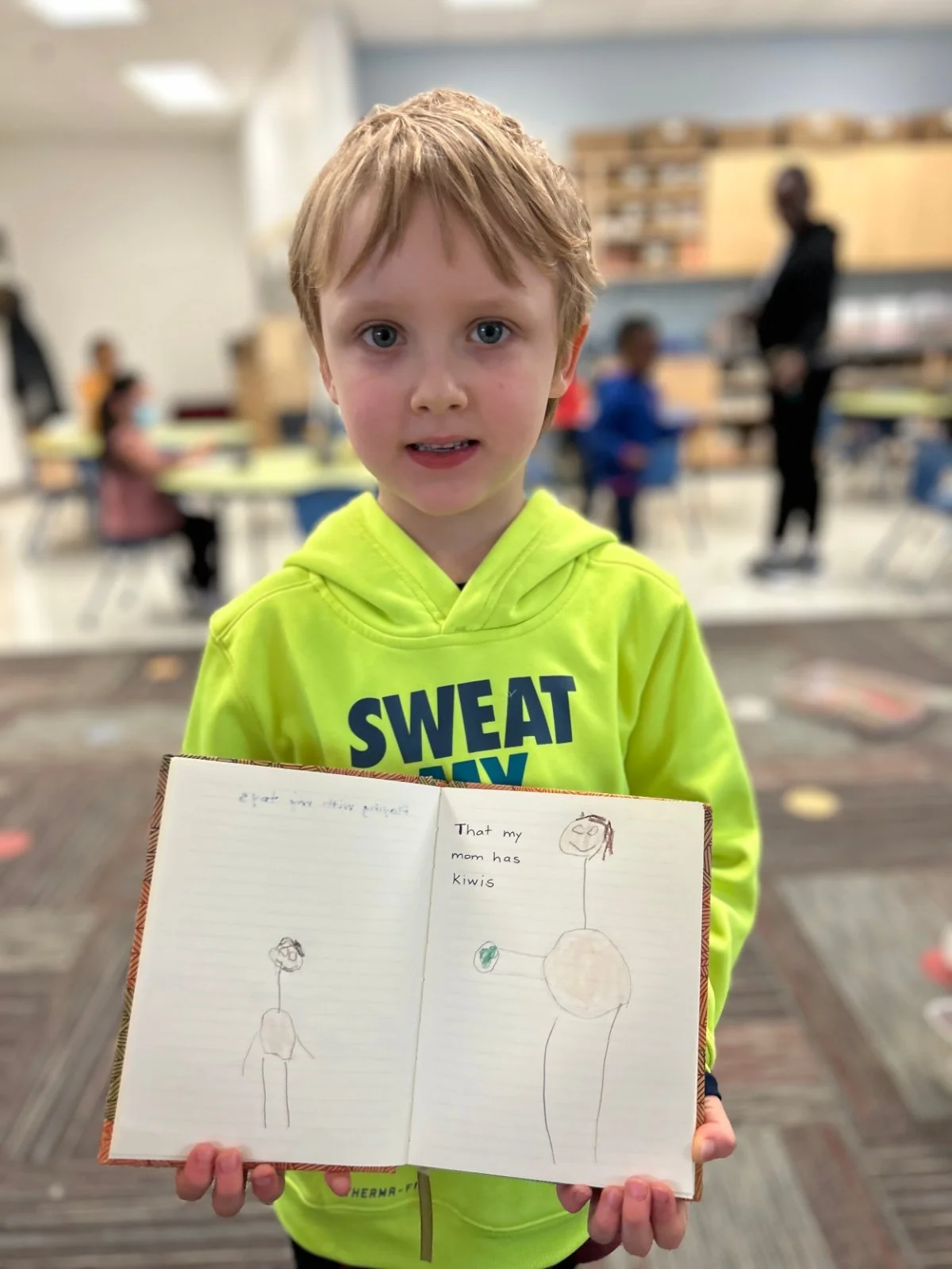 Young student in a neon yellow hoodie holding an open Gratitude Journal in a classroom