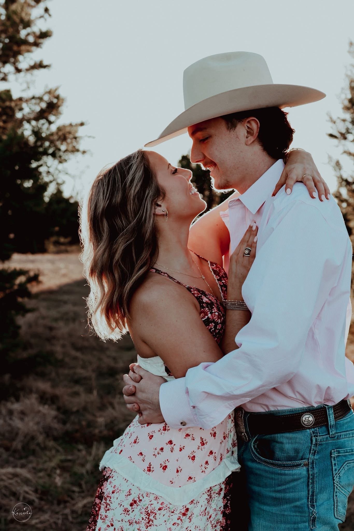 A couple embracing outdoors during sunset, smiling and looking into each other's eyes.