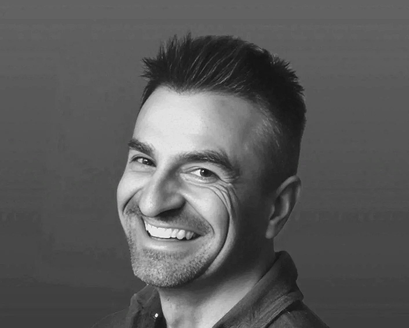 Black and white portrait of a smiling man with short dark hair, showing his teeth, against a plain background.