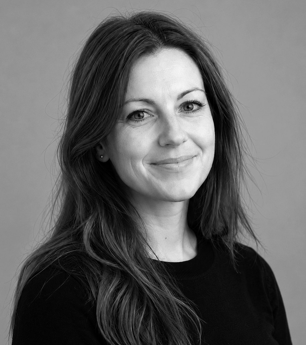 Black and white portrait of a woman with long wavy hair, smiling softly, wearing a black top, against a plain background.
