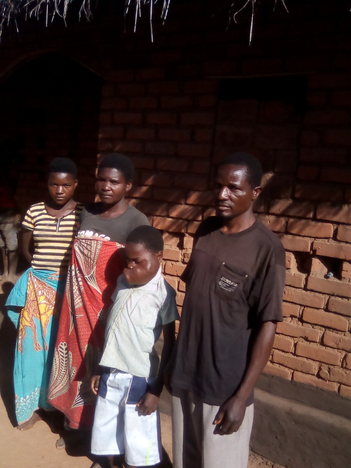 Mphatso stands with his family in front of their home in Mozambique.