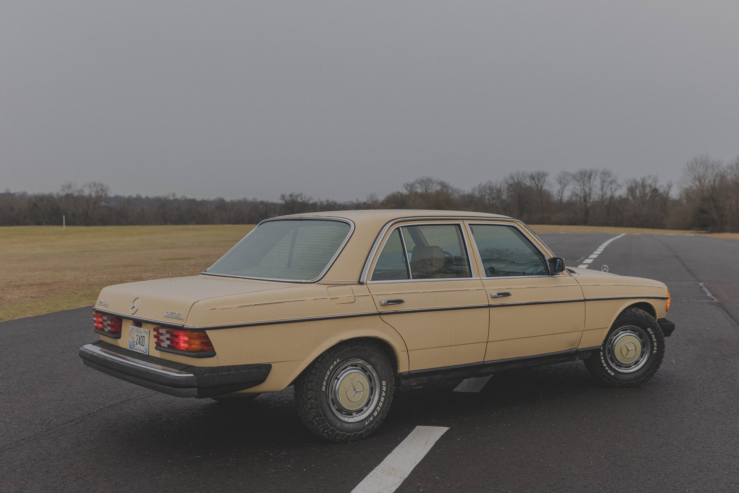 Vintage beige Mercedes-Benz 240D car parked on a road with overcast sky.
