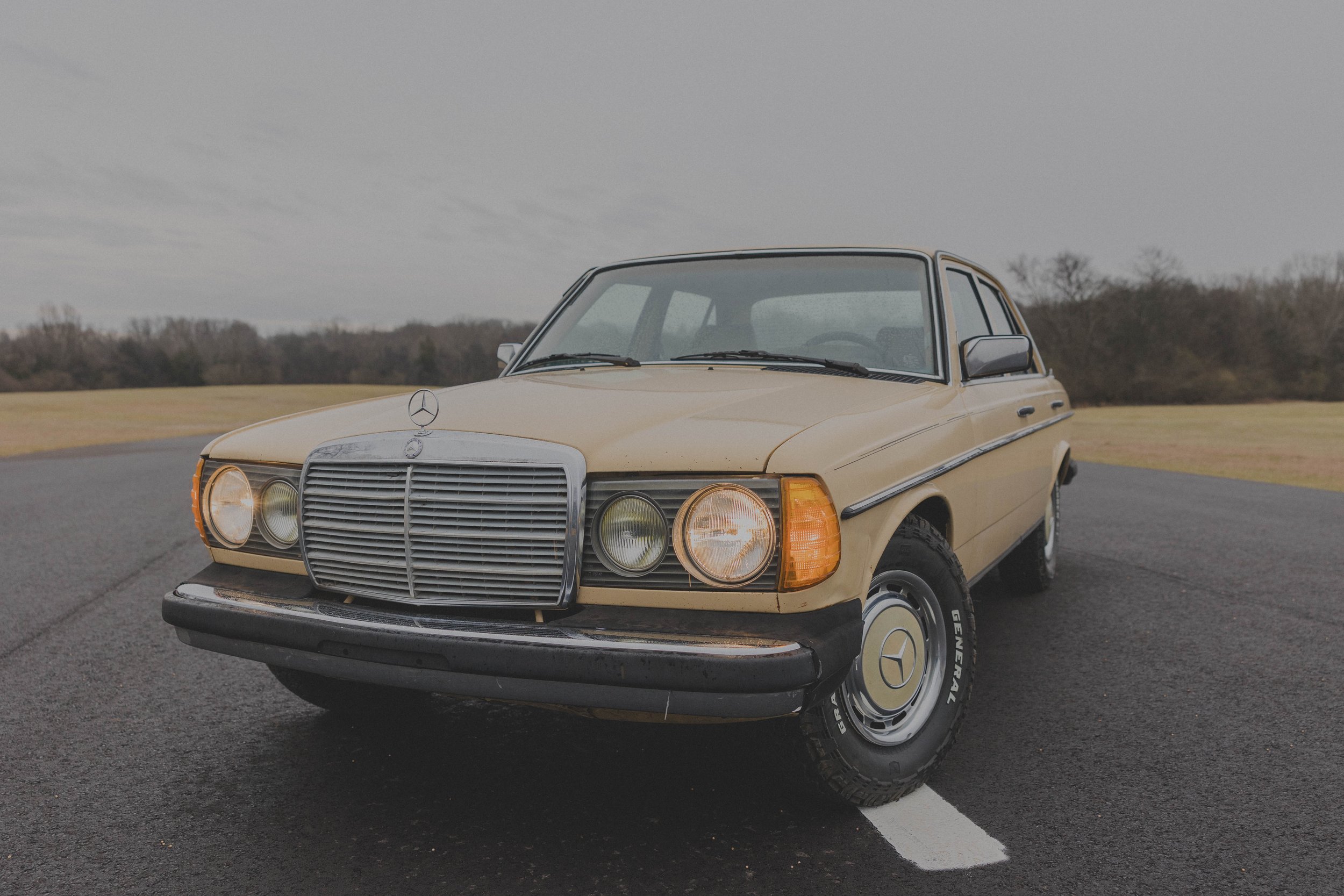 Vintage beige Mercedes-Benz car on an asphalt road with grassy surroundings.