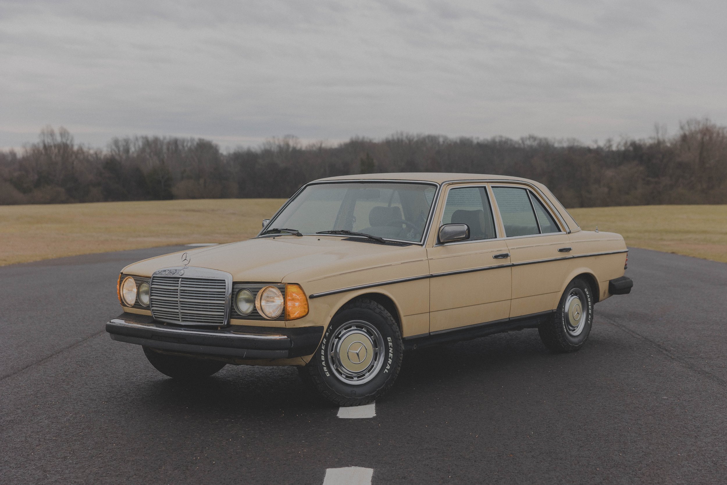 Vintage beige Mercedes-Benz sedan on a paved road with trees in the background.
