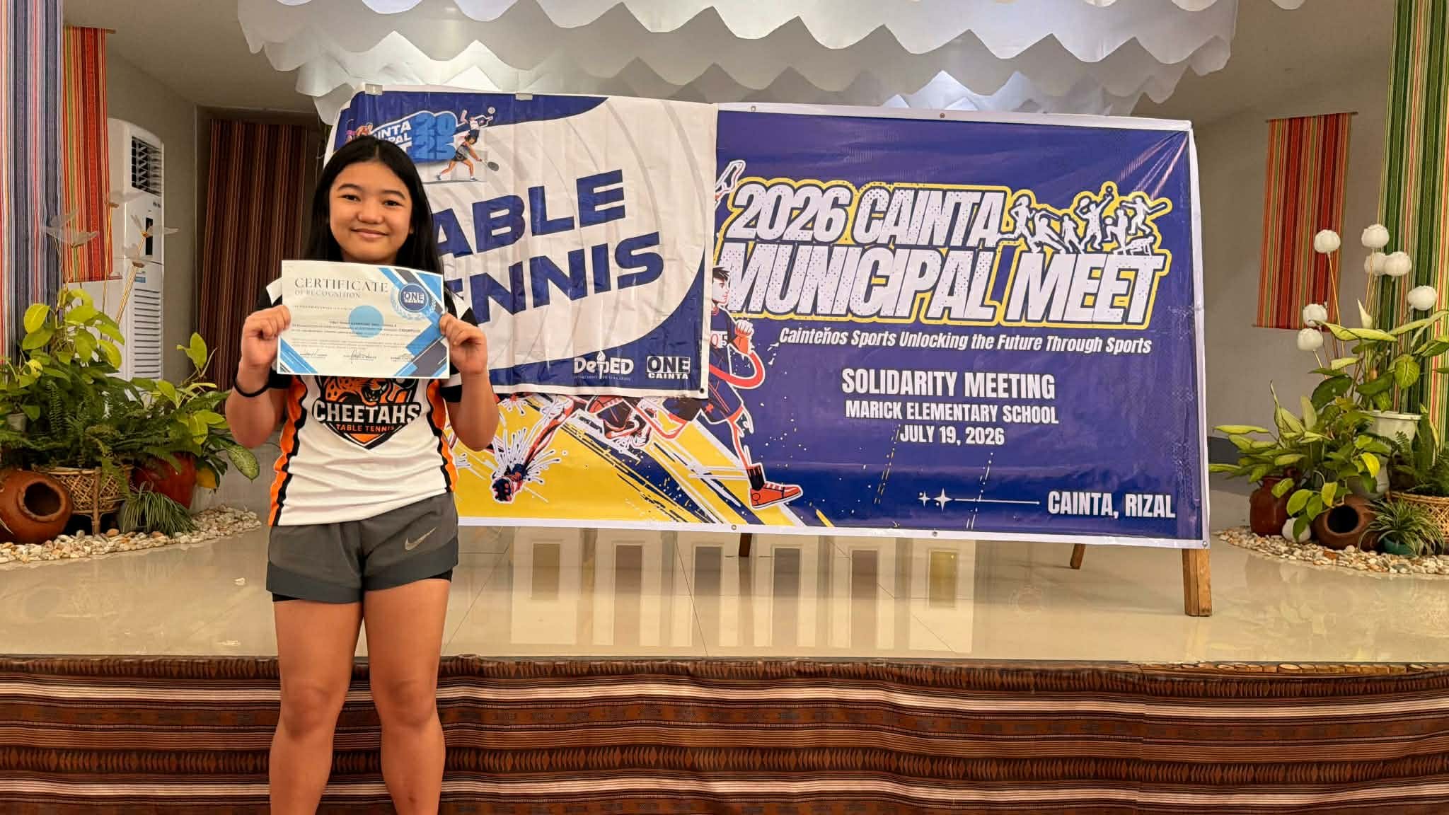 Gabrielle Santiago holds her certificate beside the 2026 Cainta Municipal Meet table tennis banner at Marick Elementary School in Cainta, Rizal.