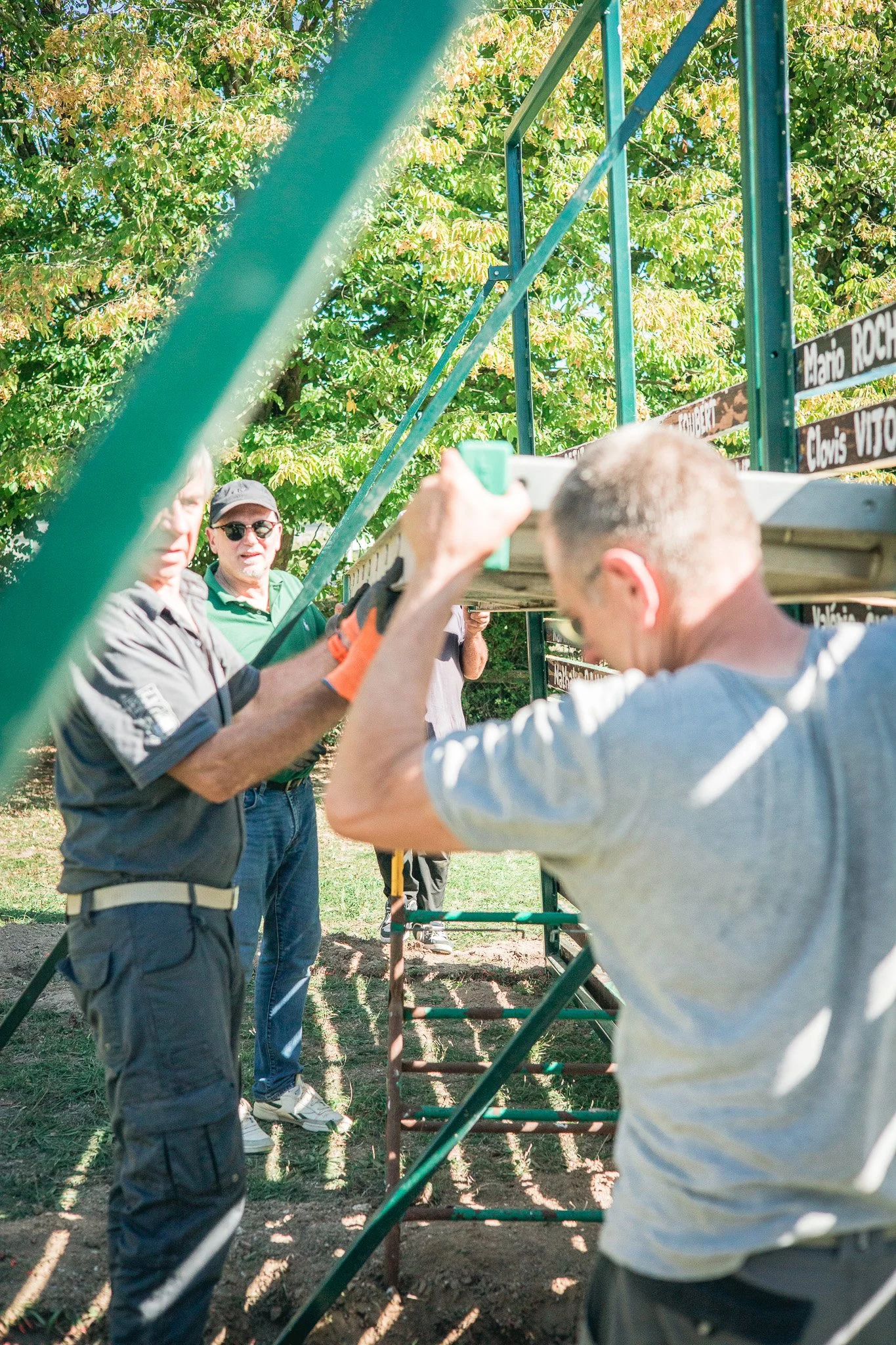 Groupe de personnes participant à une activité en plein air, entourées de verdure, à côté d'une structure en métal avec des panneaux nominatifs.