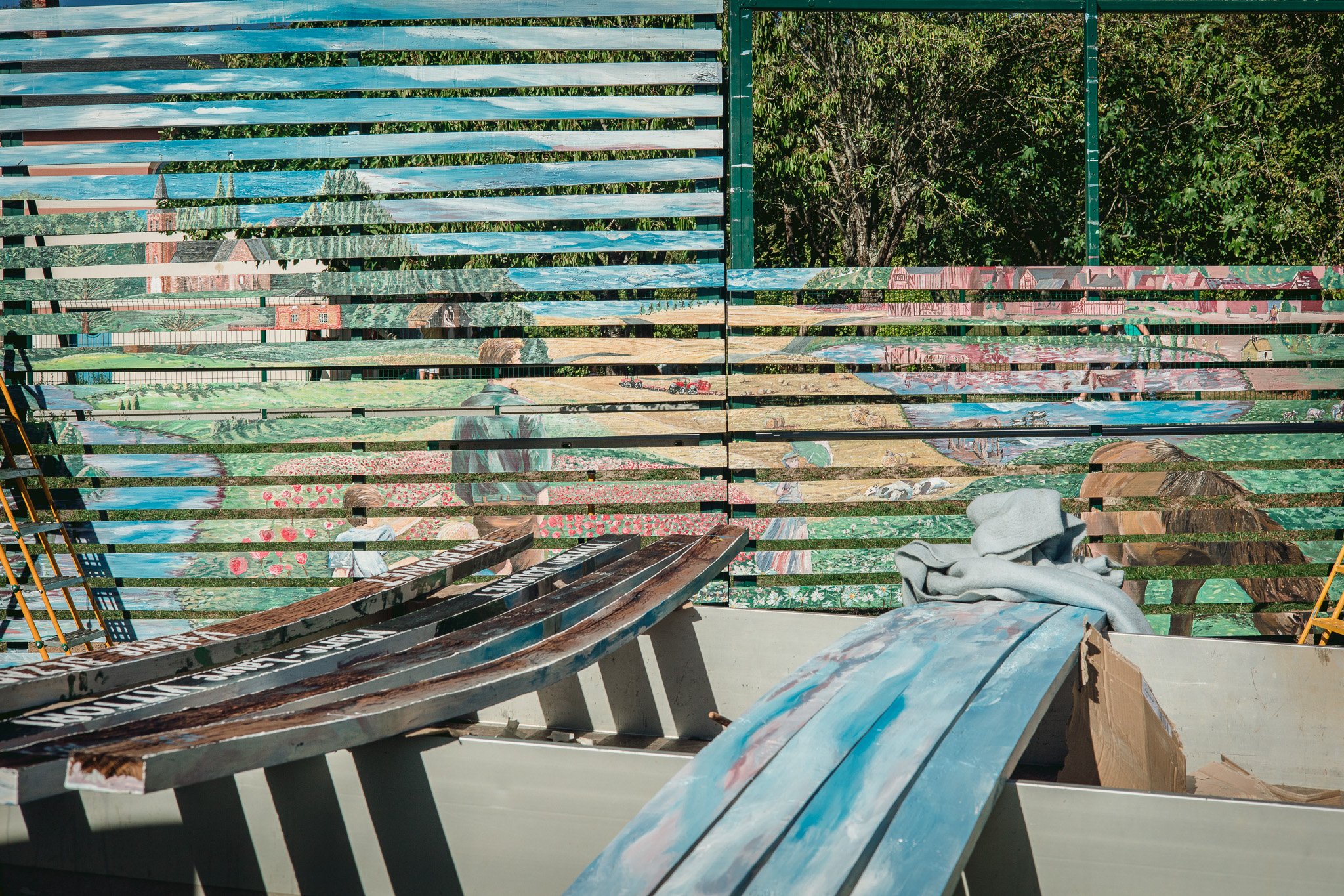 Bancs en bois peints avec des motifs de nature et de bâtiments, dans un espace extérieur en plein air.