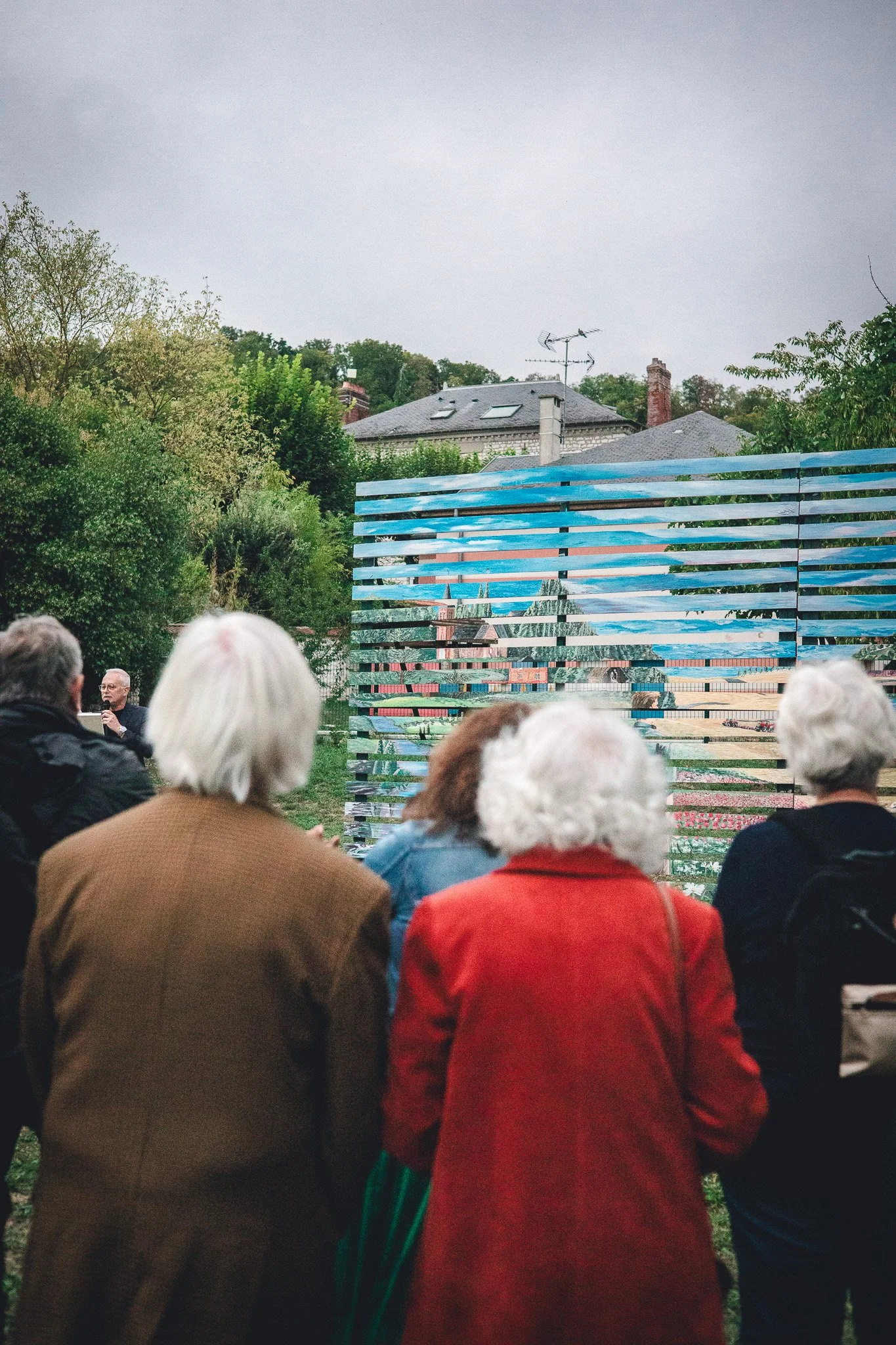 Groupe de personnes assises dans un jardin en regardant un mur mural avec des bandes de peinture colorée.