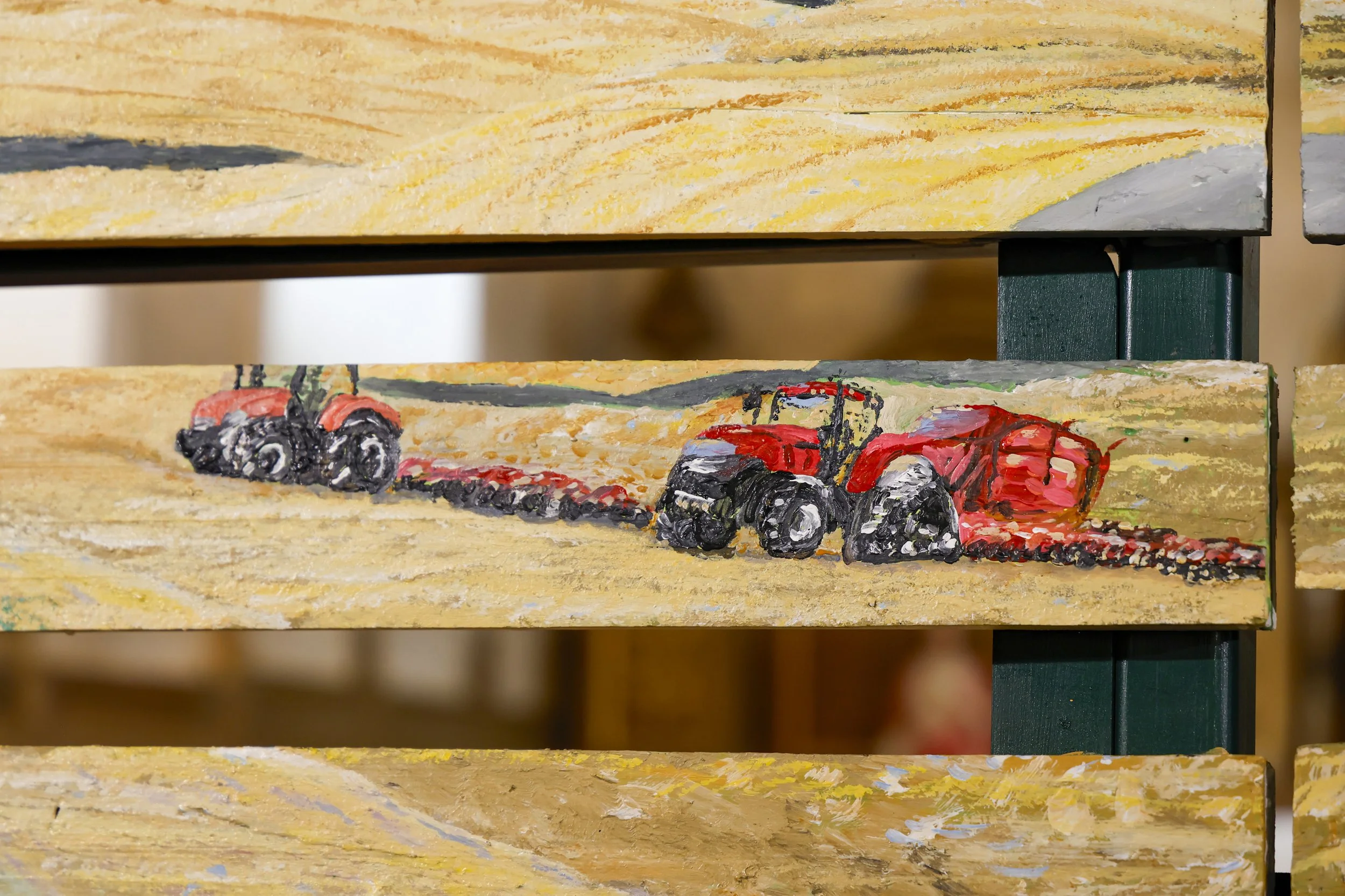 Peinture représentant un tracteur rouge dans un champ, avec un ciel gris, apparent sur un bois peint.