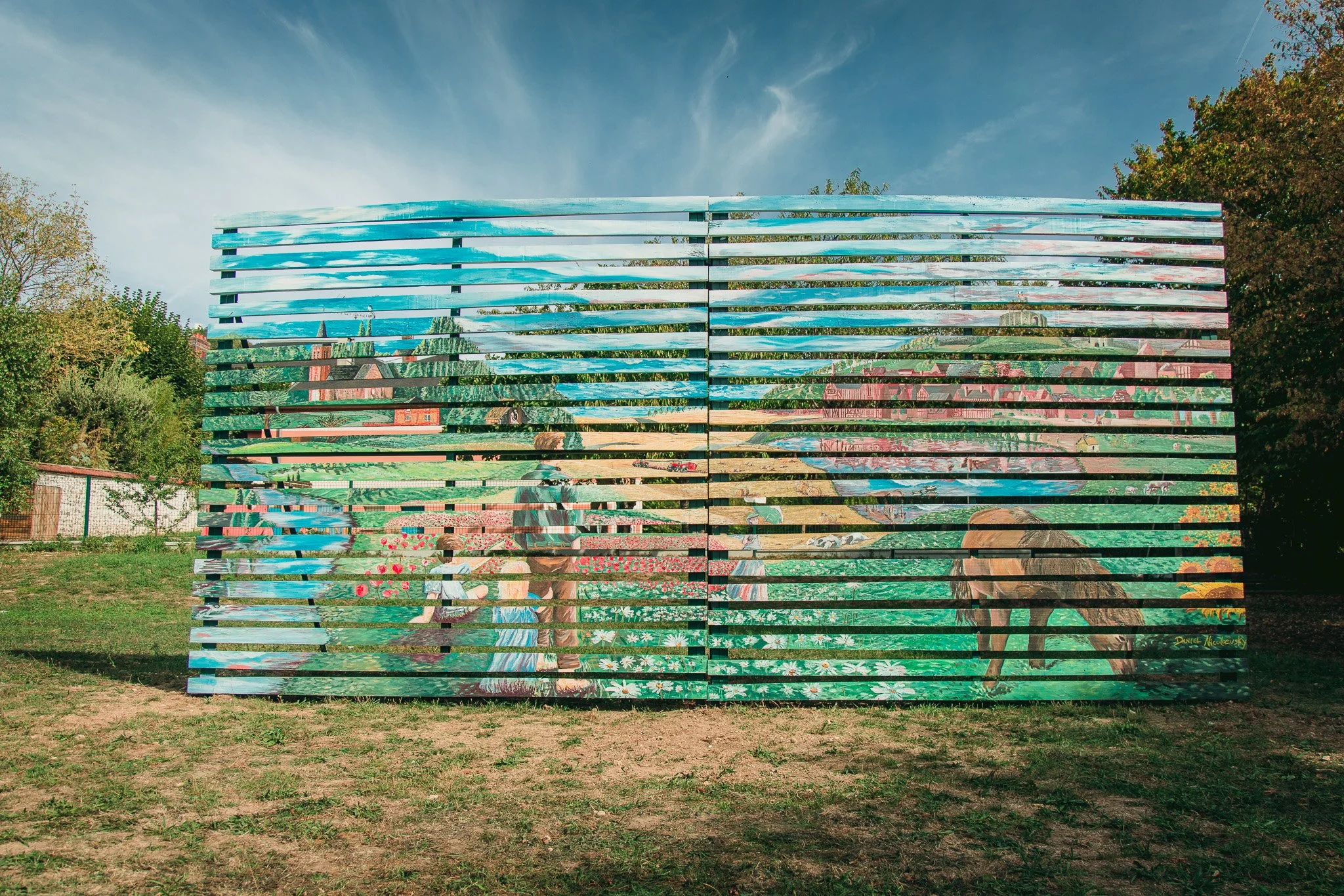 Une œuvre d'art murale réaliste de style peinture représentant un couple d'ouvriers agricoles avec un chien, dans un champ de fleurs, avec un village en arrière-plan, et composée de bandes horizontales refletant le paysage environnant.