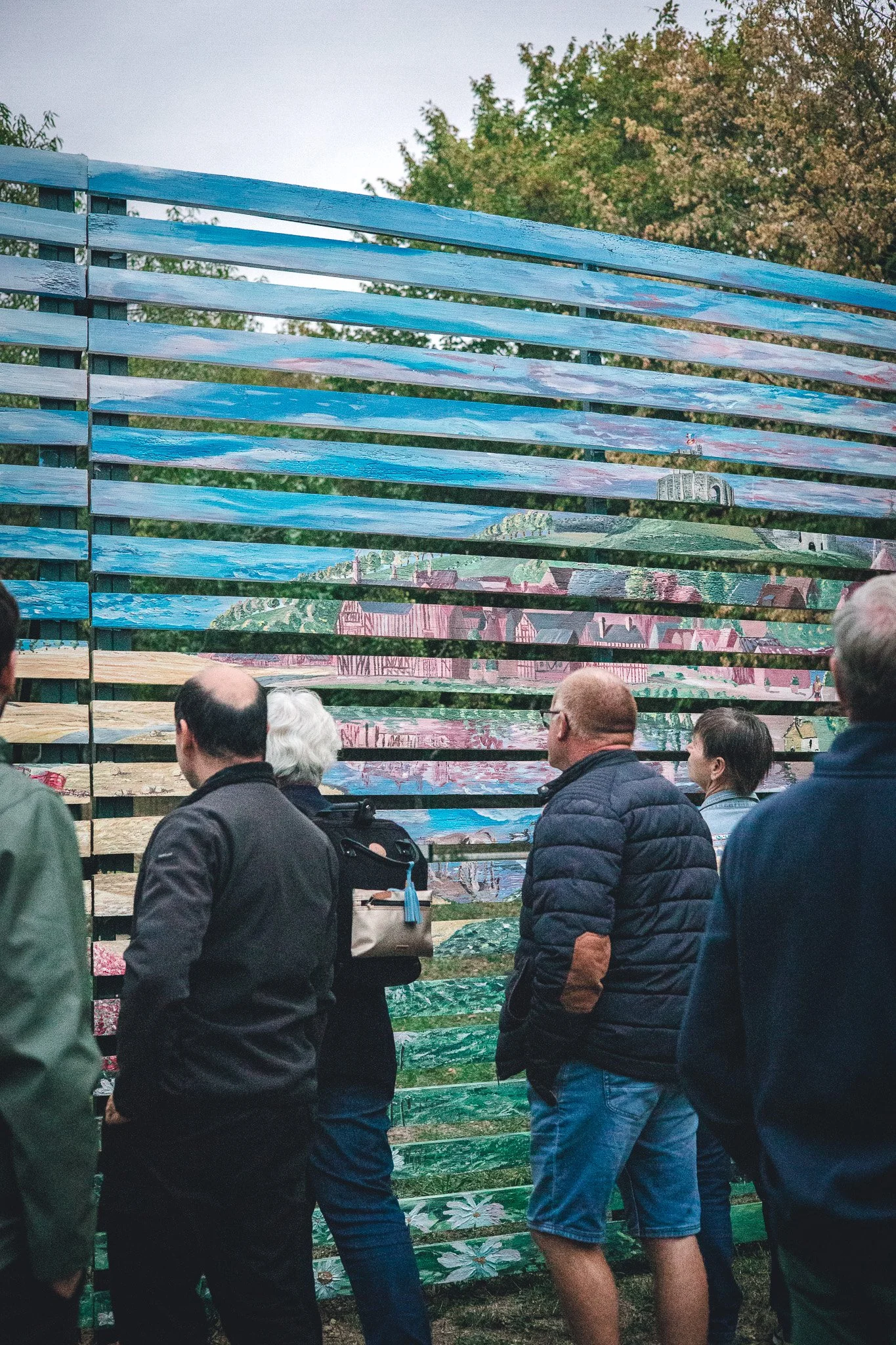 Un groupe de personnes debout devant un mur en bois peint avec un paysage de ville et de nature.