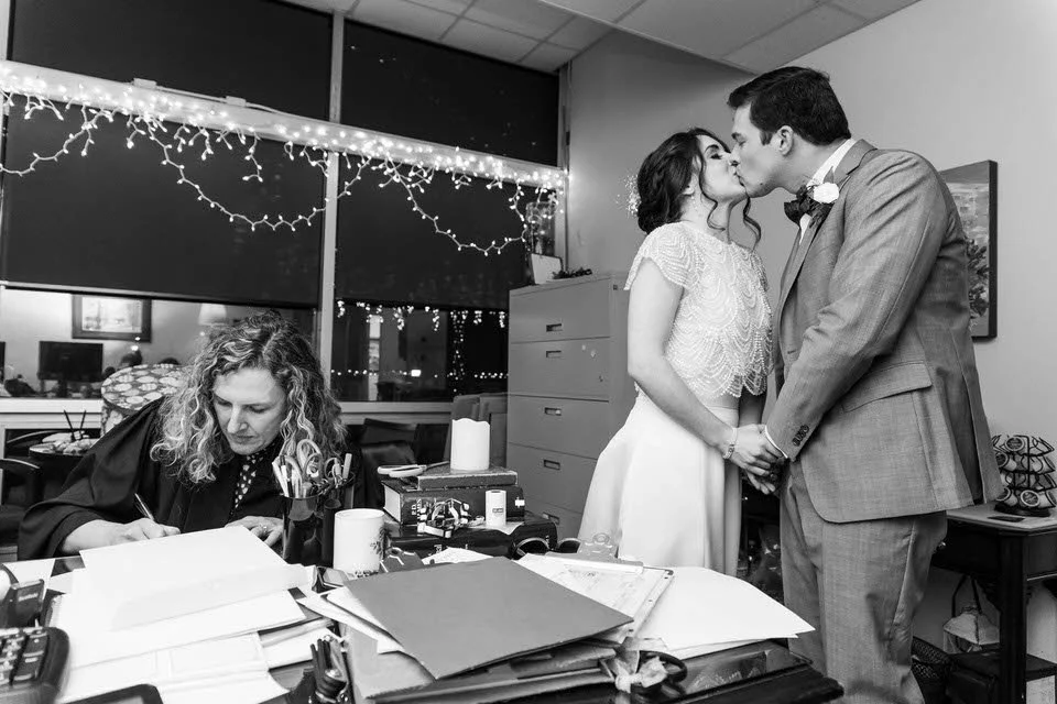 Couple kissing after ceremony while officiant signs wedding license.