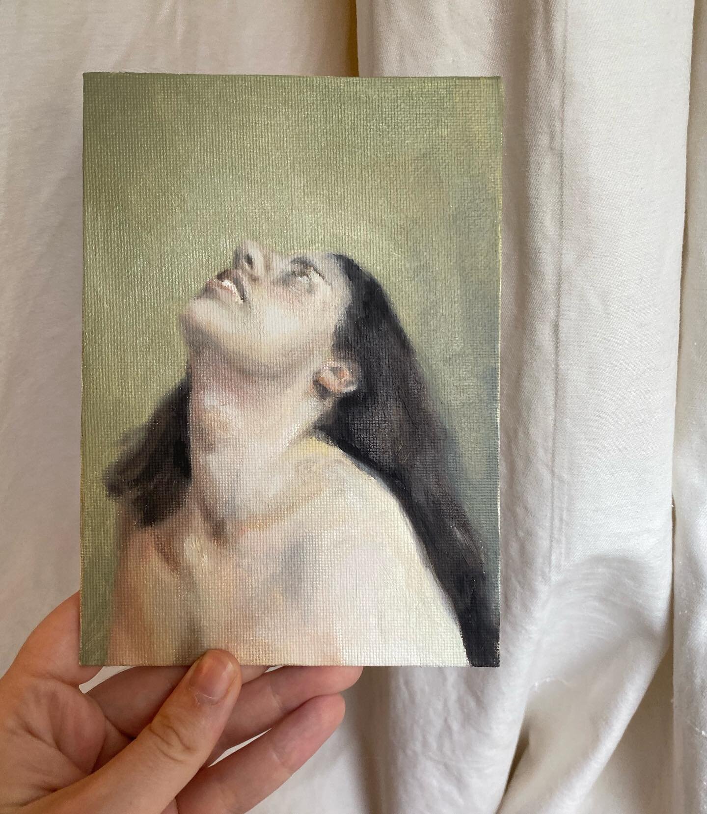 Oil sketch on canvas board.  I unexpectedly feel in love with the background colour. 

Image Description:
Image 1:
A hand is holding a small canvas board with an oil painting sketch of a white woman with brown hair. The painting shows the woman from 