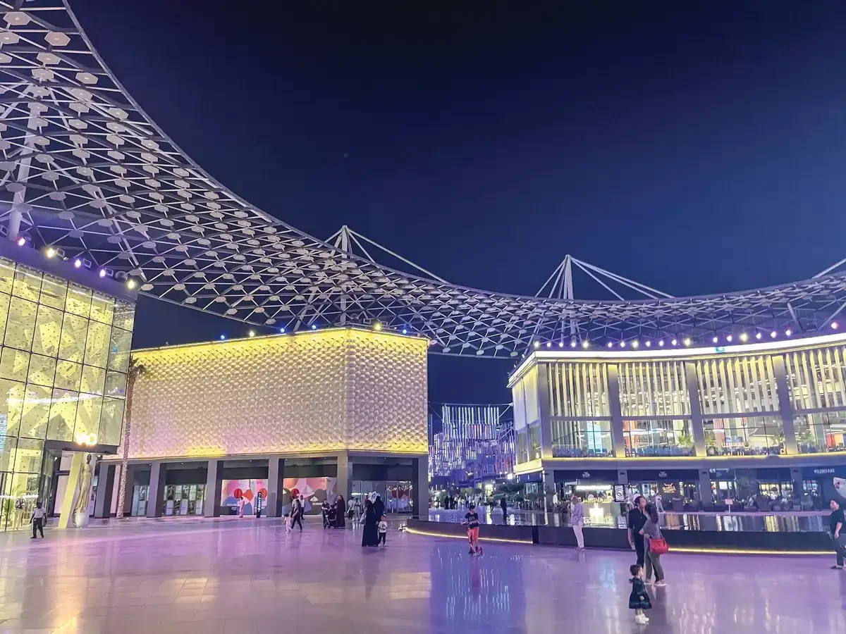 A modern outdoor plaza at night beneath a large, arched tensile canopy.