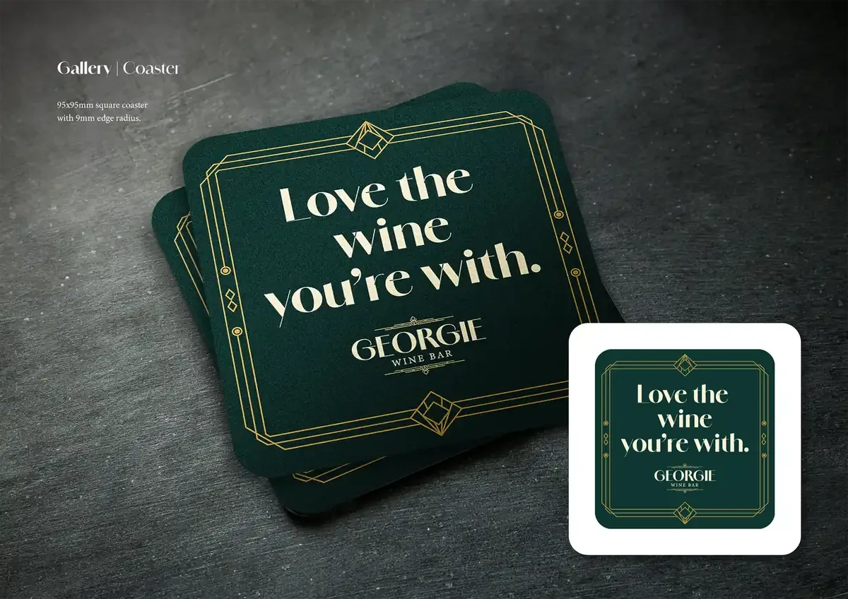 Green square coasters with gold geometric border and the phrase ''Love the wine you're with'' in white serif font, for George Wine Bar, displayed on a dark surface.