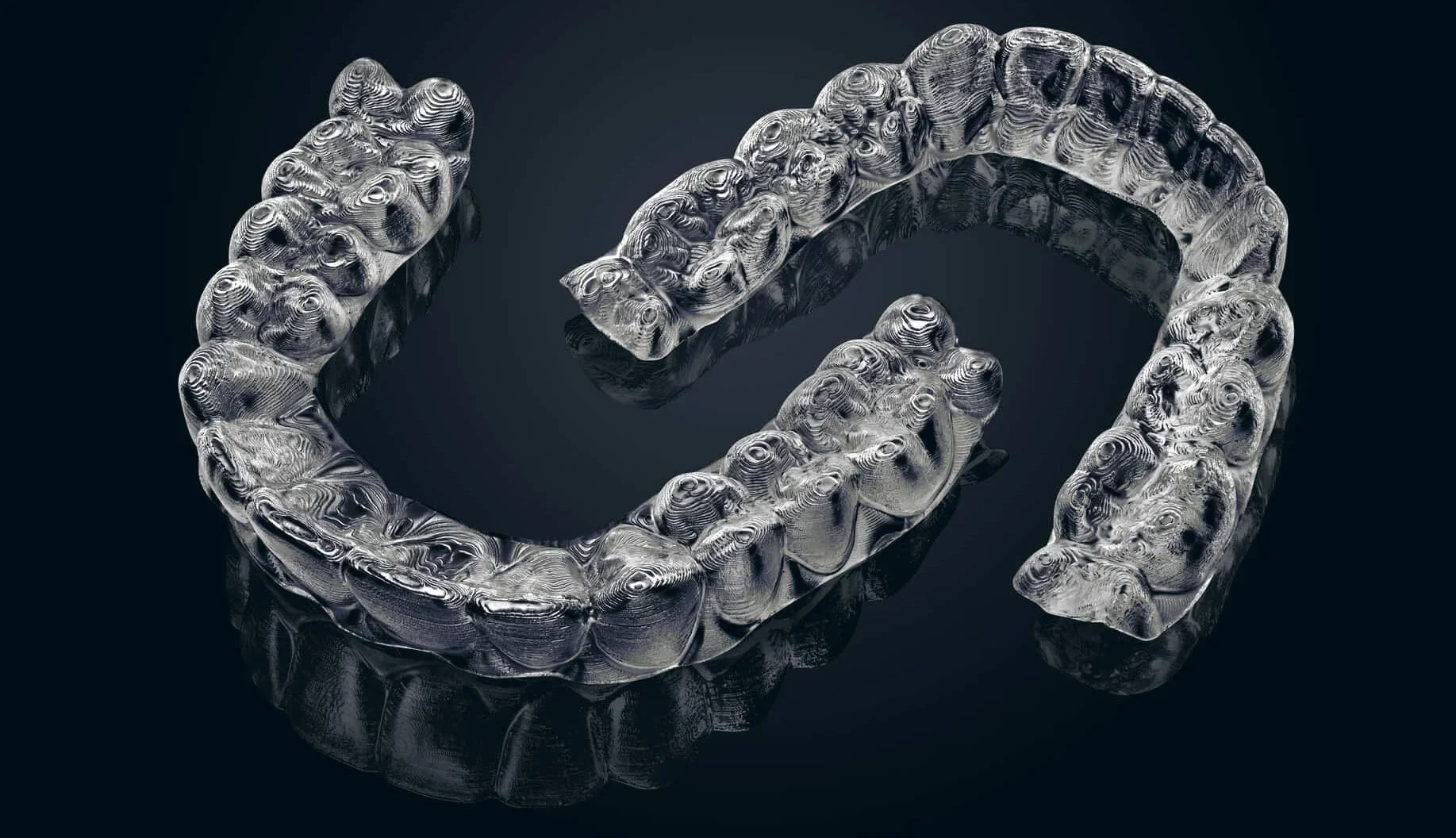 A silver, textured, spiral-shaped jewelry piece with a glossy finish, displayed against a black background and reflecting underneath.