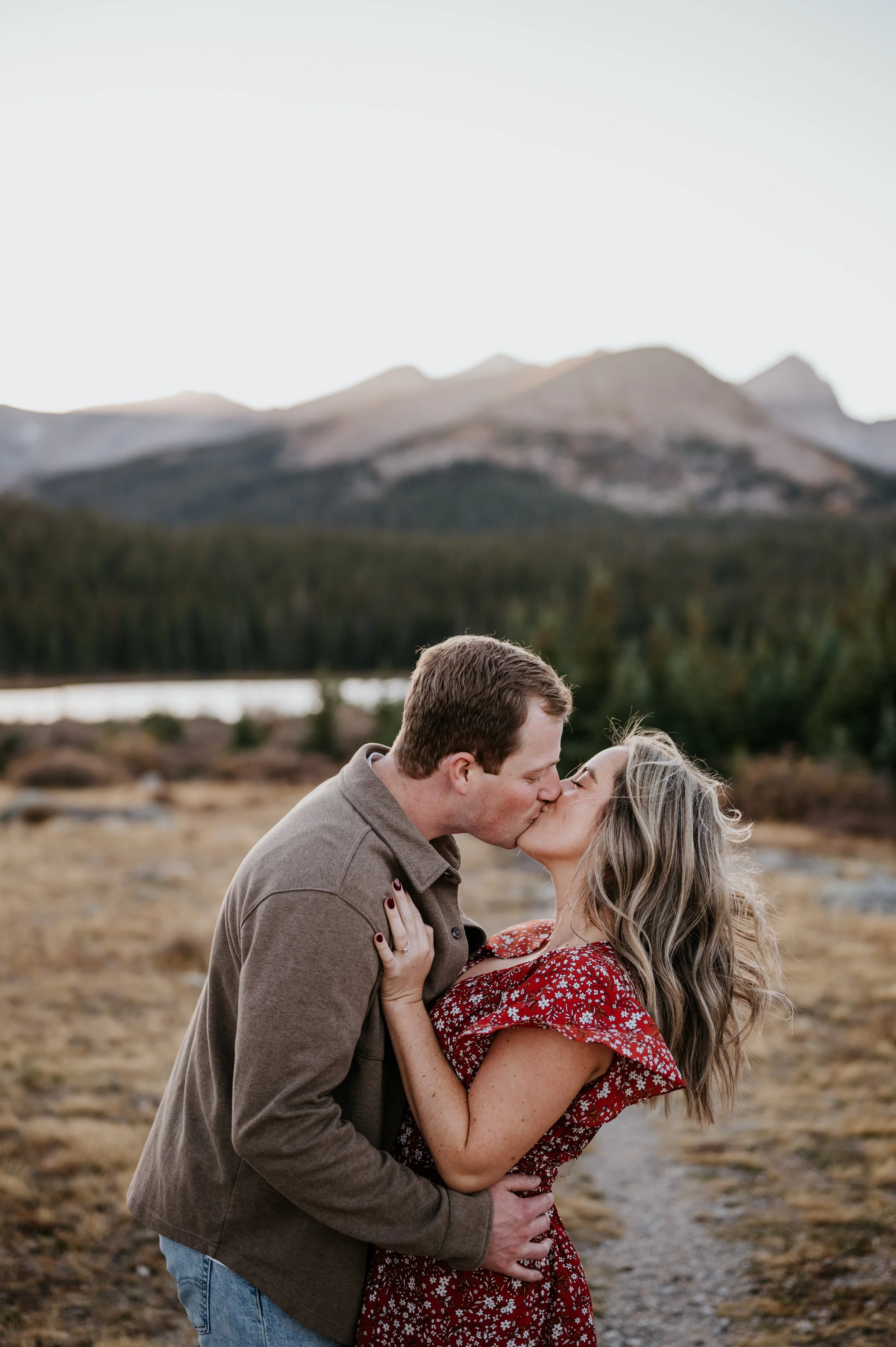 A couple kissing outdoors in a mountain landscape with trees and a lake in the background. Colorado wedding photographer, Denver wedding photographer, colorado elopement photographer, film wedding photographer denver