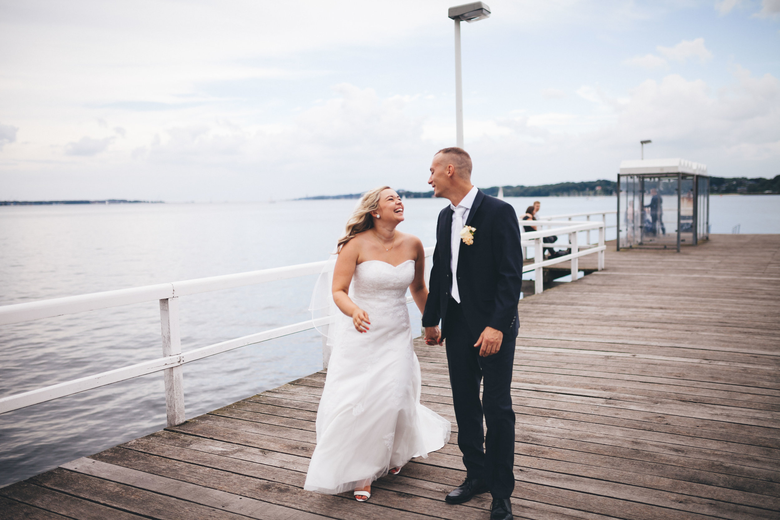 Ein Hochzeitspaar läuft über das Steg der Seebar Kiel und schaut sich dabei lachend an. Sie sind frisch verheiratet und Glücklich. Fotografier im rahmen einer Hochzeit von Phil Schreyer 2016