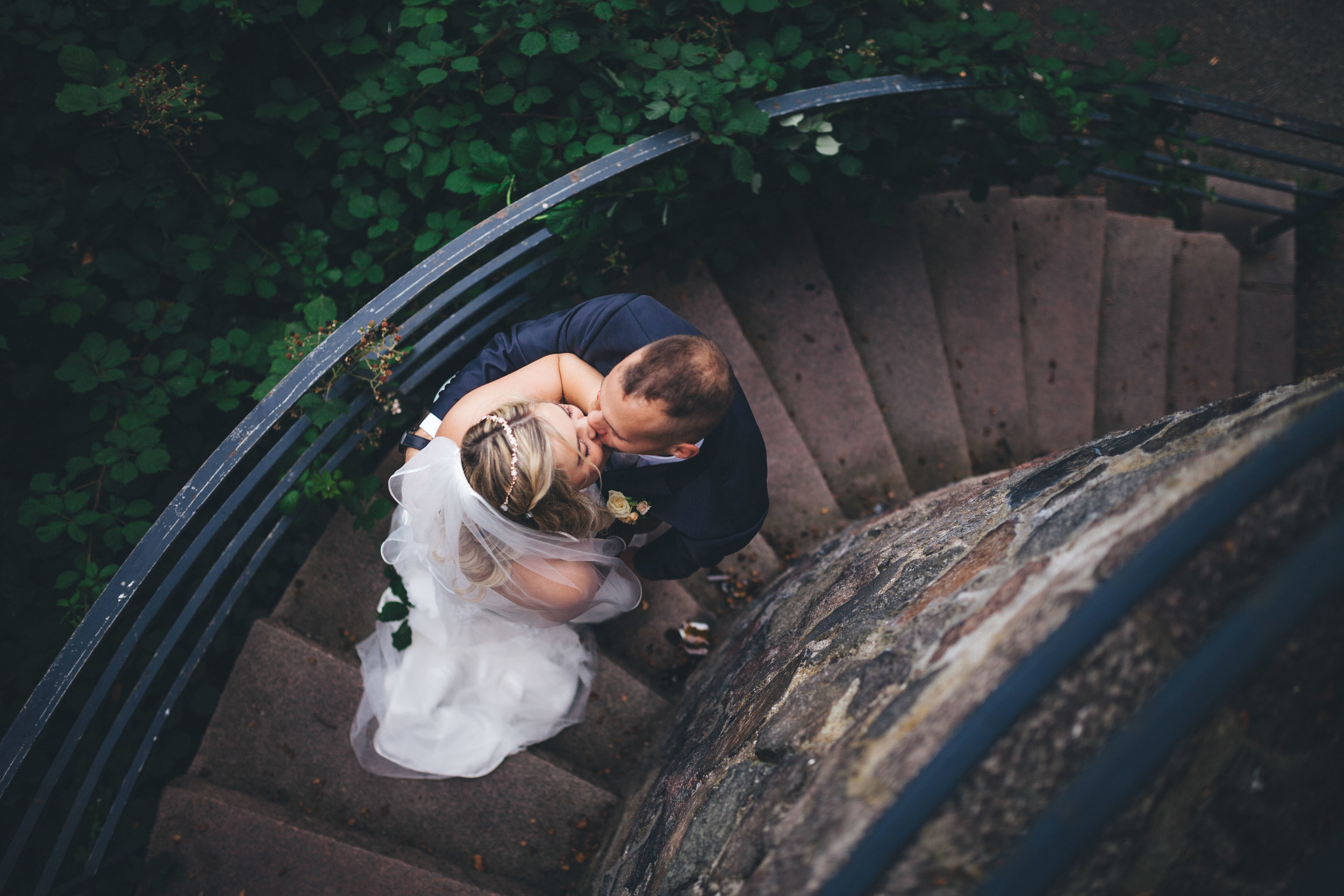 Ein Hochzeitspaar gibt sich auf einer Wendetreppe im Wald einen Kuss. Fotografiert von Oben bei einer Hochzeit von Phil Schreyer