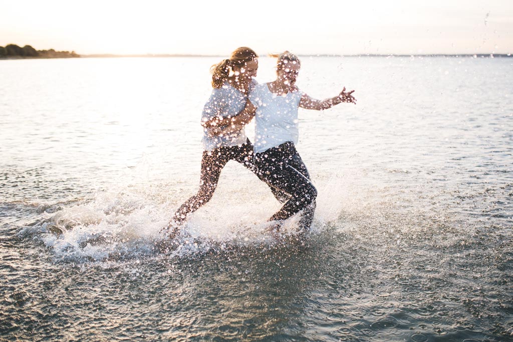 zwei freundinen laufen am Strand im Ortsteil Stein von Kiel, durchs Wasser. Im Hintergrund geht die Sonne unter. Das Foto entstand bei einem Freundinen Fotoshooting in Kiel von Fotograf Phil Schreyer.