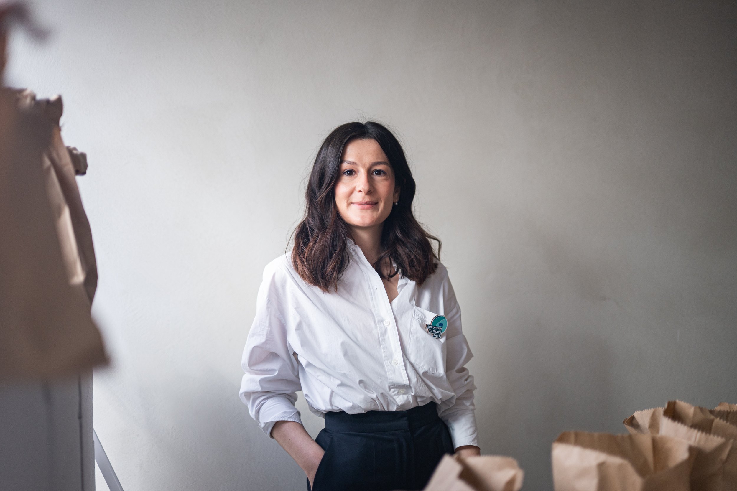 Woman in a white shirt standing indoors next to paper bags.