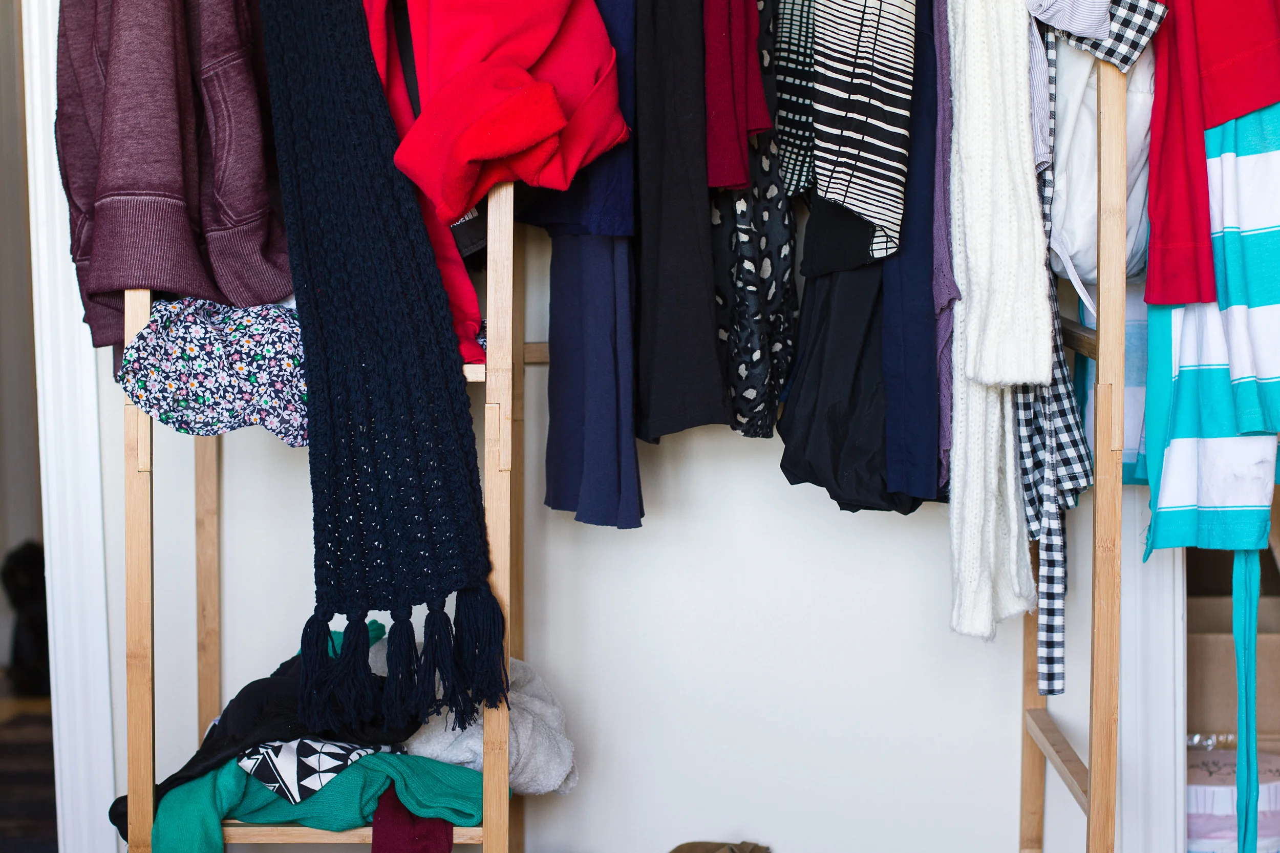 Clothes hanging on a wooden rack, including patterned shirts, sweaters, and jackets.