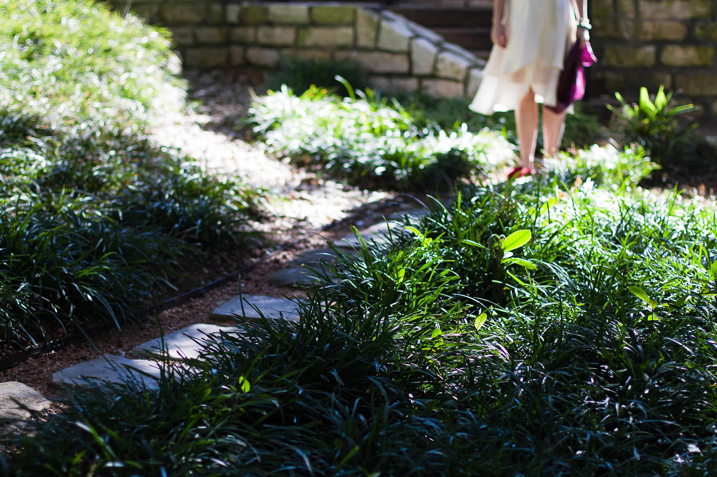 Two women standing near a stone staircase surrounded by lush green bushes and plants in a garden.