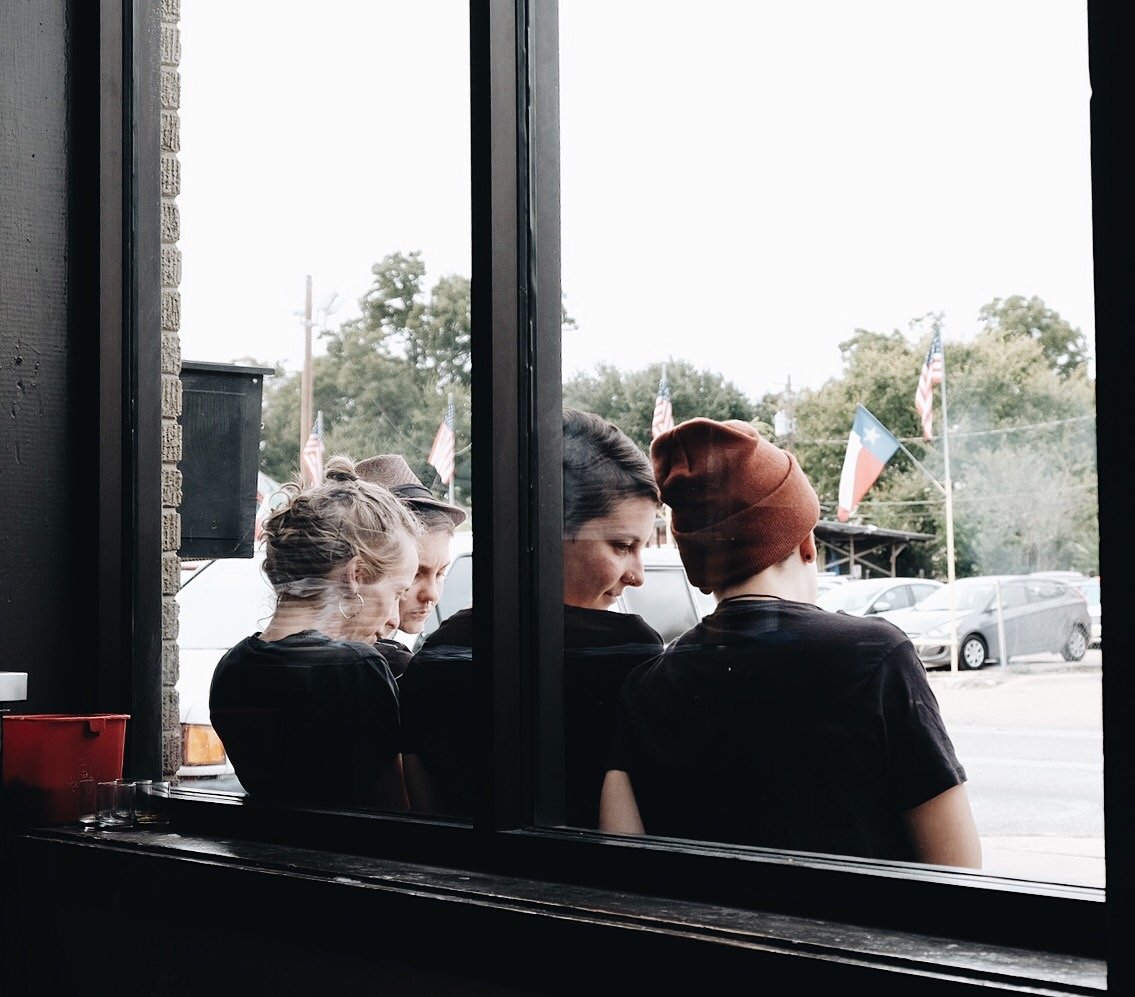 Four people sitting outside viewed through a window, with American and Texas flags in the background.